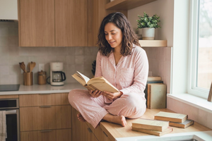 Mujer con pijama rosa de pantalón lee sobre la encimera de una cocina, ejemplo de homewear para mujer con estilo en casa.